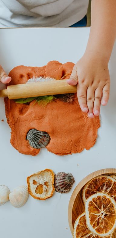 Enfant utilisant un rouleau avec de la pâte à modeler et des éléments naturels